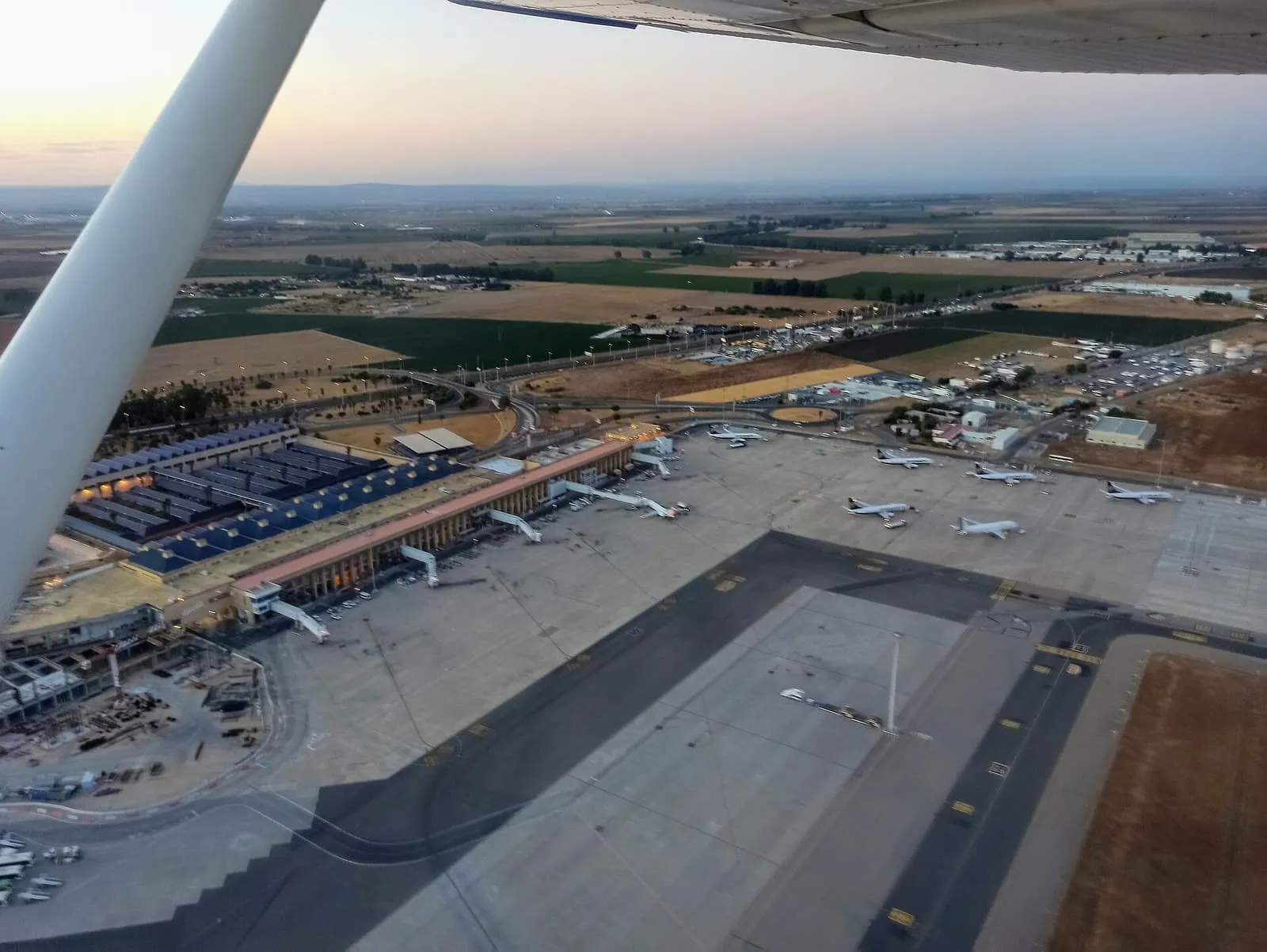 Terminal und Vorfeld des Flughafens Sevilla aus einem startenden Flugzeug, umgeben von Feldern