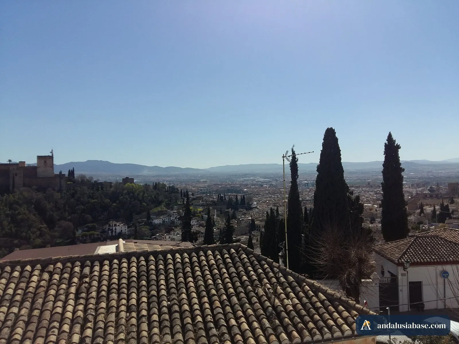 A Alhambra e montanhas ao longe, para lá dos telhados e dos altos ciprestes do Albaicín