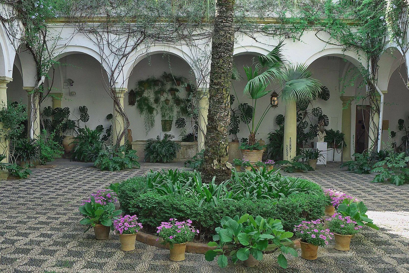 Pátio com arcadas, uma palmeira e vasos de plantas no Palacio de Viana, em Córdova