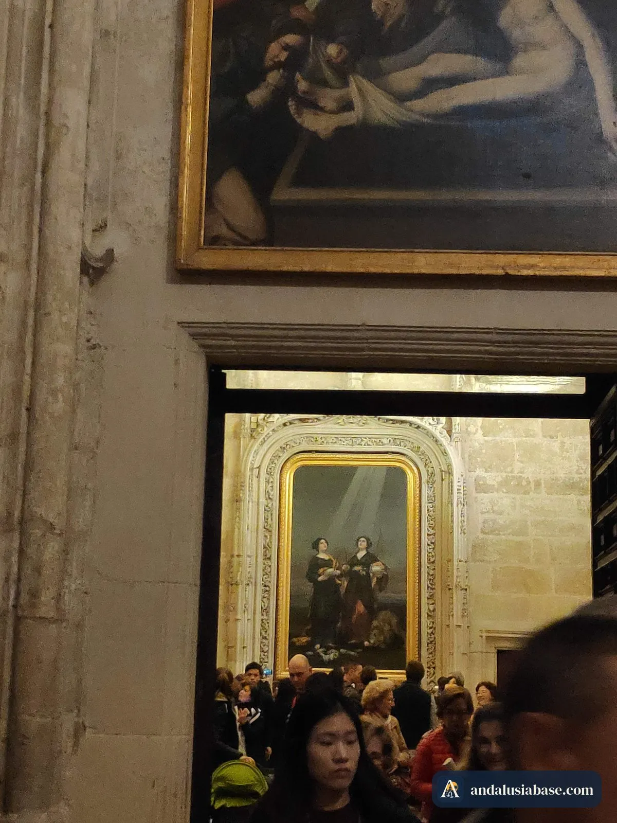 Visitors crowding the entrance of a side chapel inside Seville Cathedral, beneath a large painting
