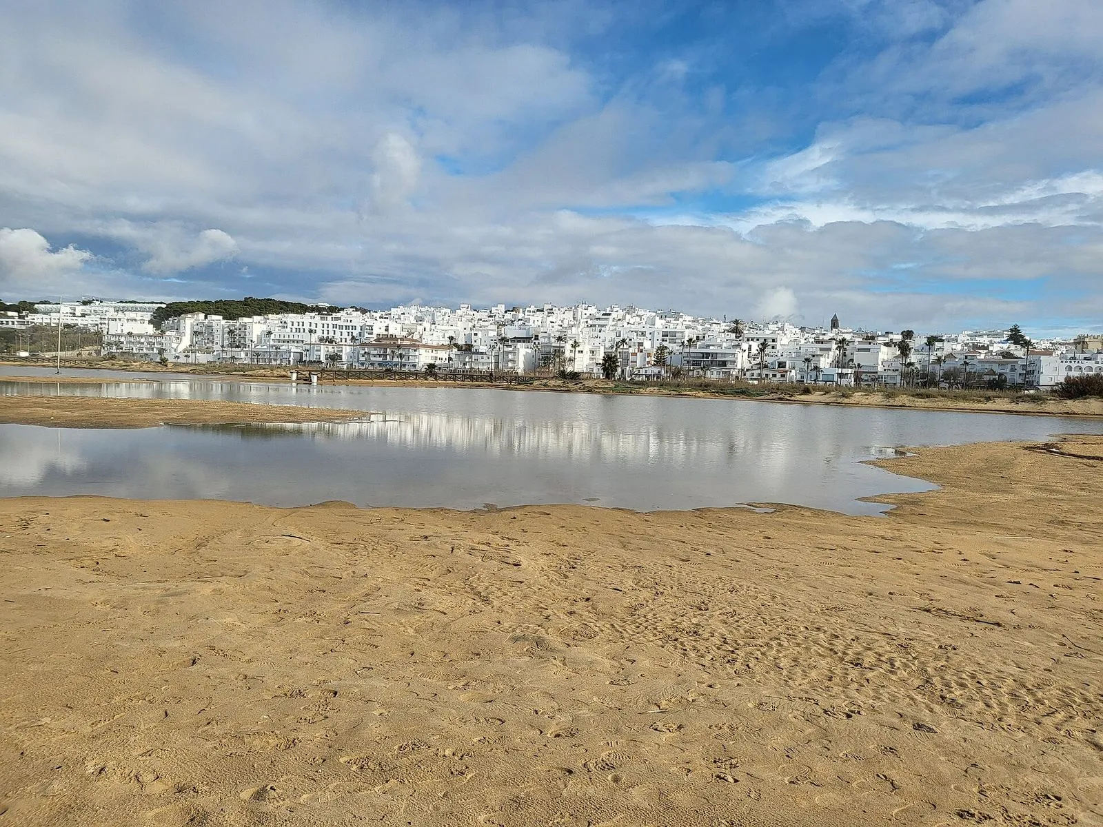The white town of Conil de la Frontera seen across the sand and river mouth at Los Bateles beach
