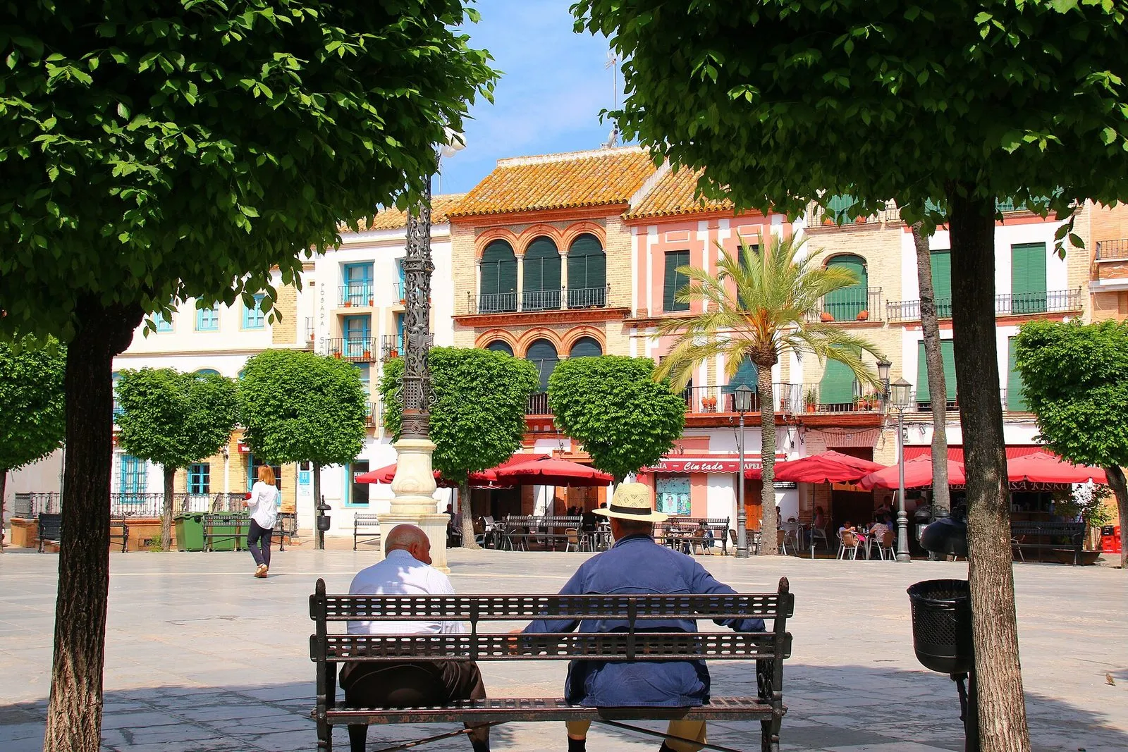 A tree-lined square in Carmona with café terraces under red parasols