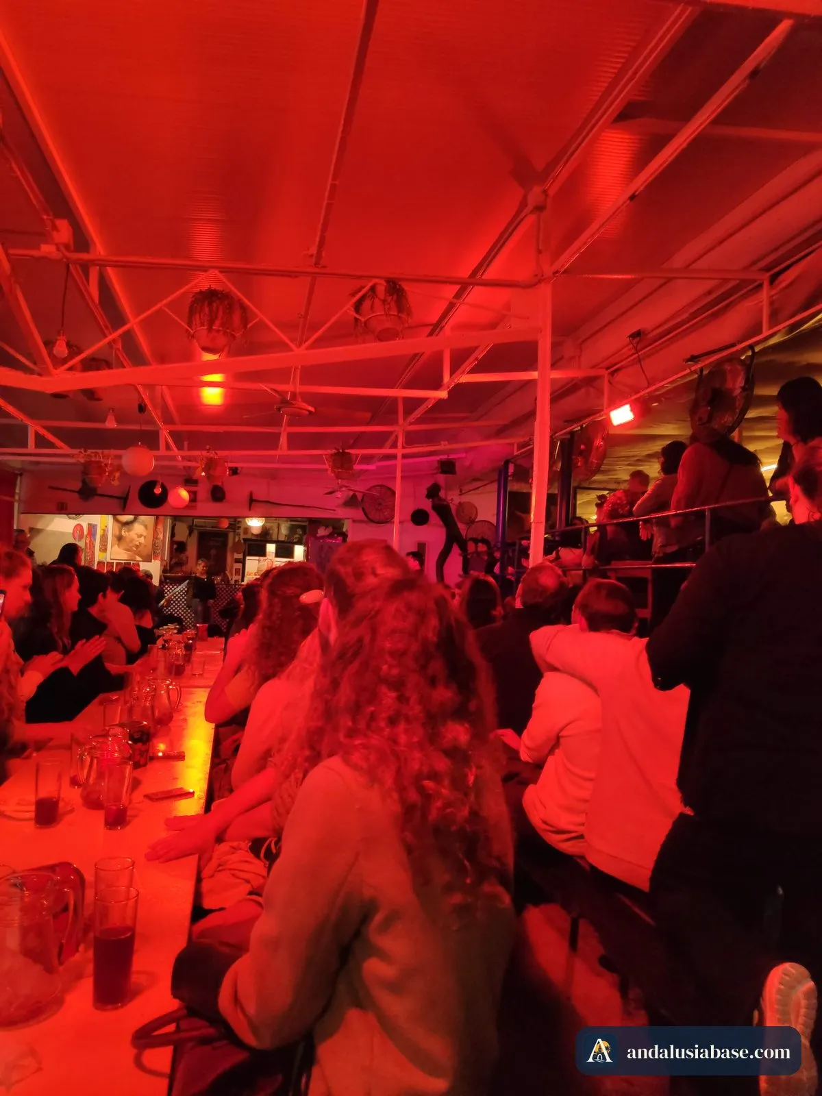 Mesas compridas cheias de gente sob luzes vermelhas em La Carbonería numa noite de flamenco
