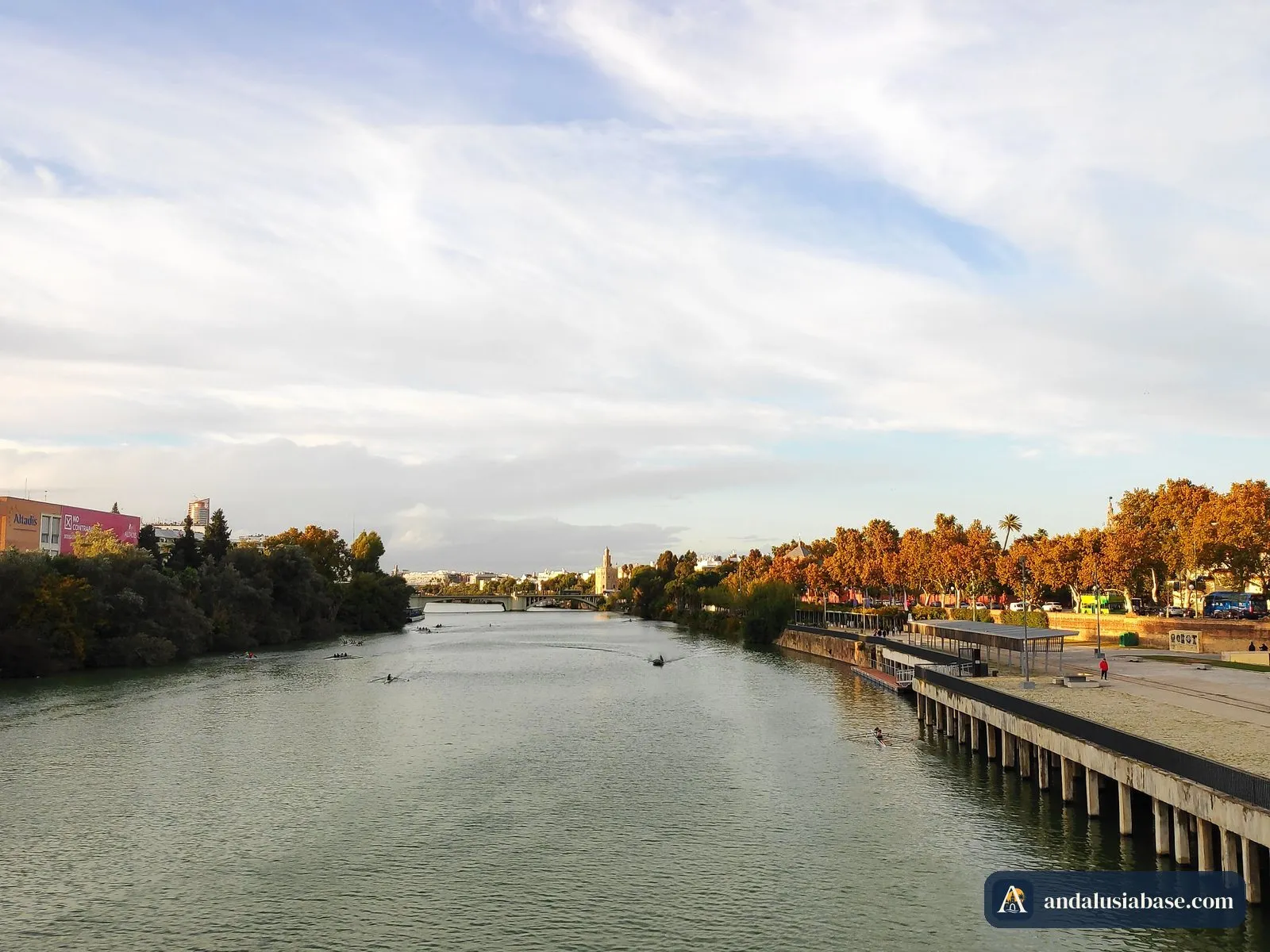 O Guadalquivir visto de uma ponte ao fim da tarde, com árvores outonais ao longo do passeio ribeirinho