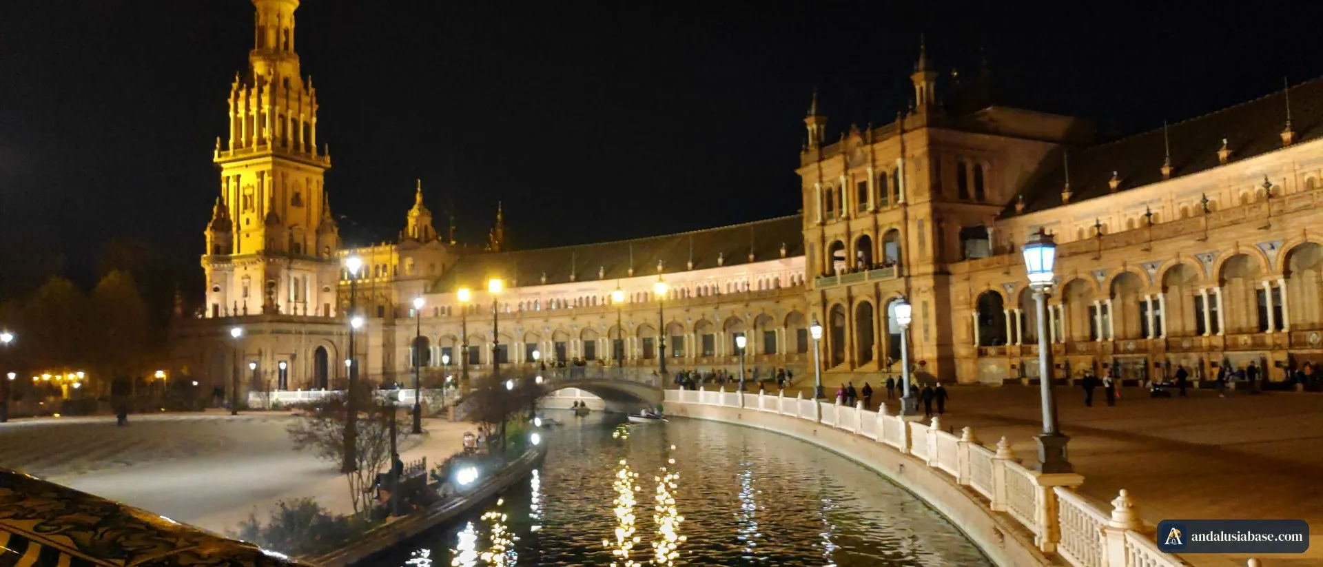 A Plaza de España à noite, com a torre e as arcadas iluminadas refletidas no canal