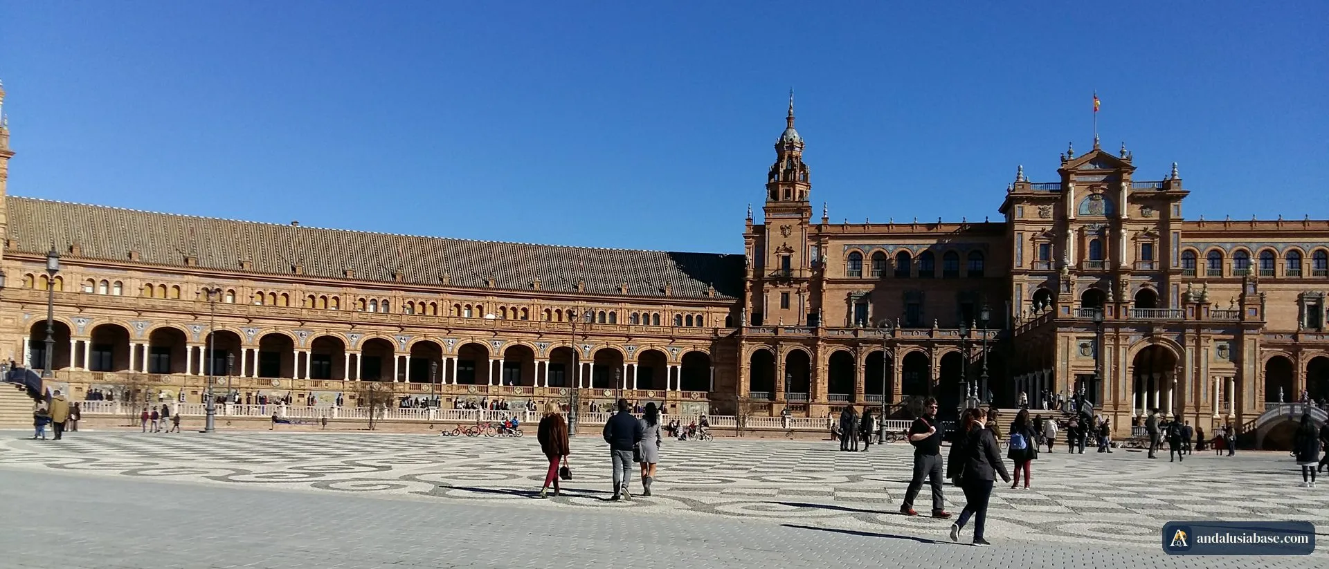 Visitantes a passear pela ampla praça calcetada da Plaza de España, em Sevilha, sob um céu limpo