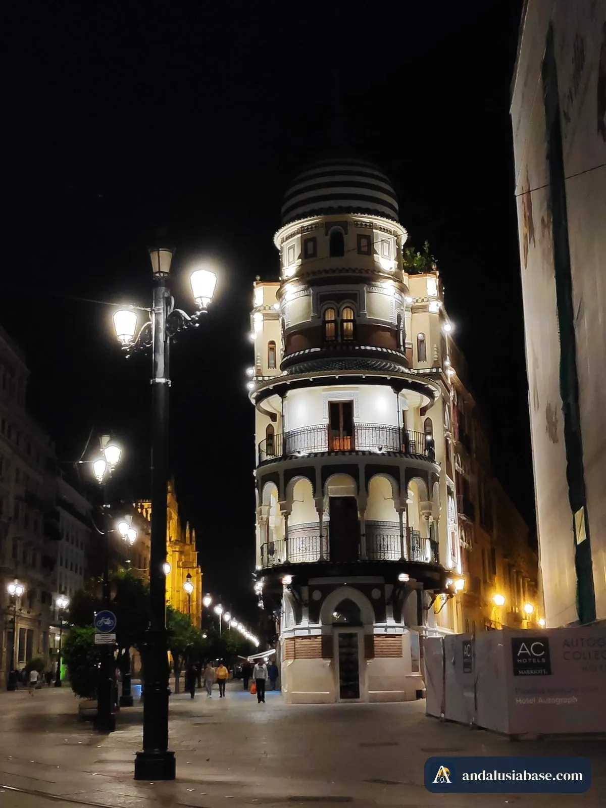 Tram tracks running along Avenida de la Constitución at night, past the La Adriática building