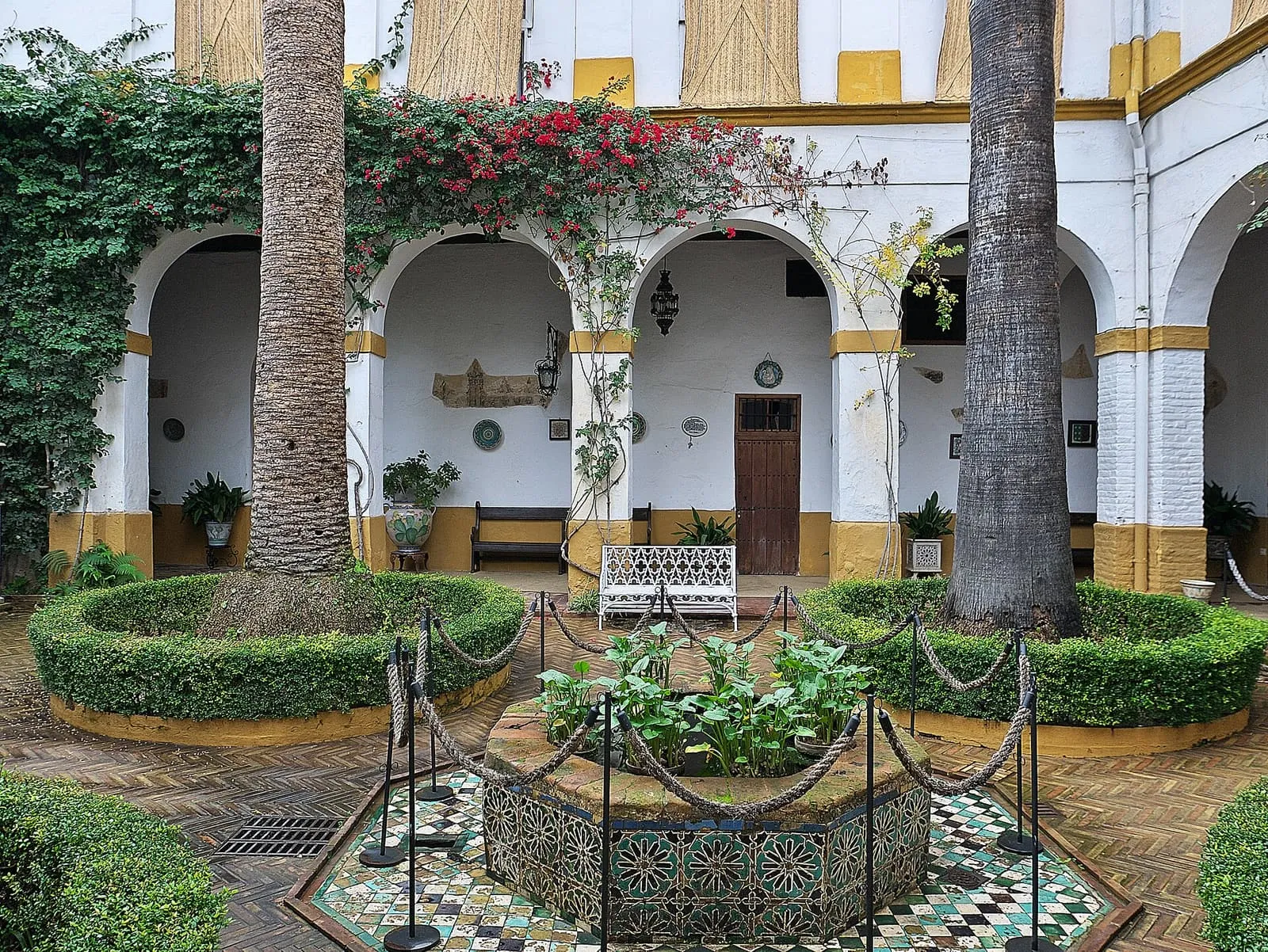 Der Patio del Aceite im Palacio de las Dueñas in Sevilla mit Palmen, Hecken und Fliesenbrunnen