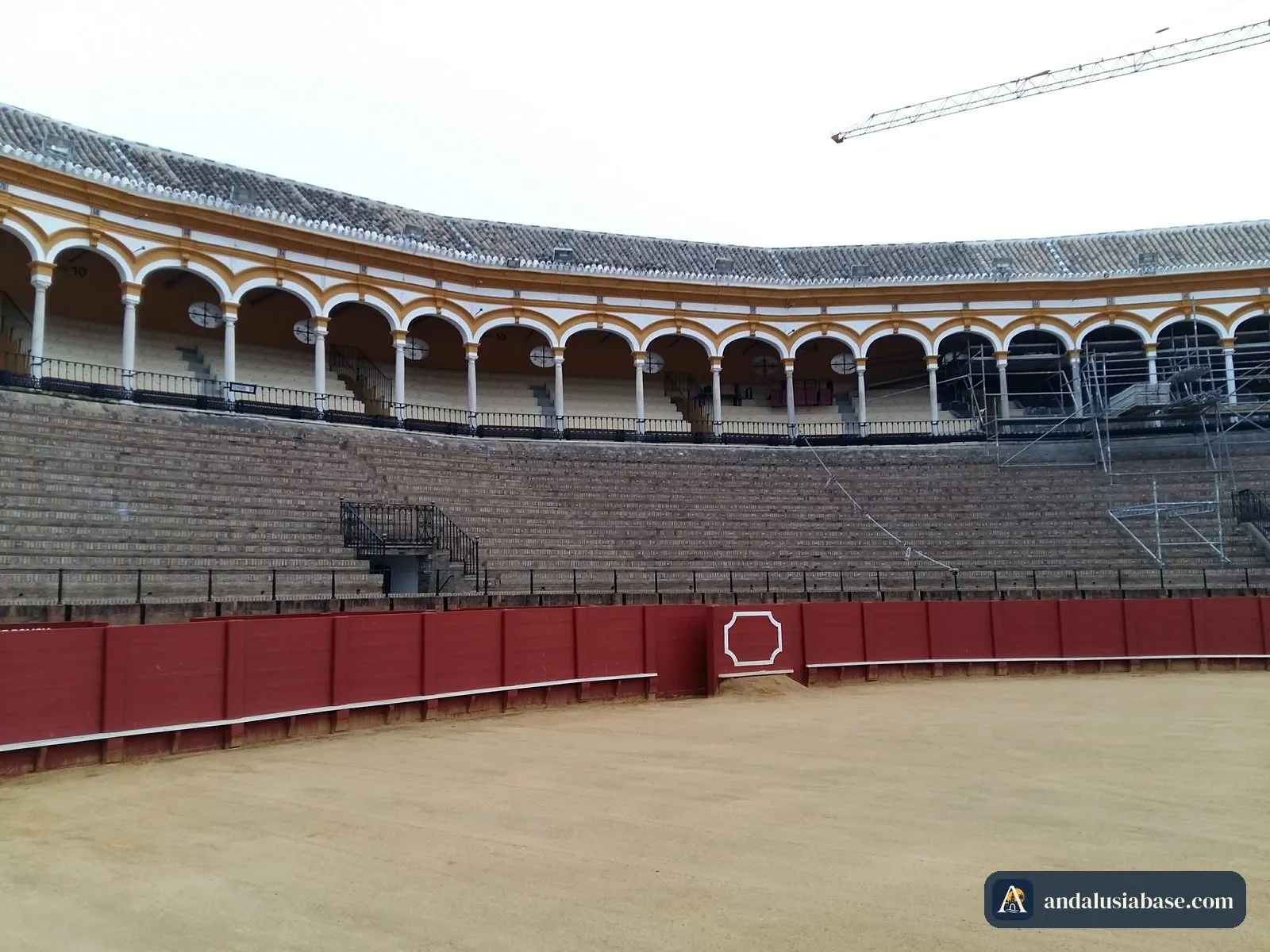 A arena de areia, a barreira vermelha e as bancadas com arcadas da Maestranza