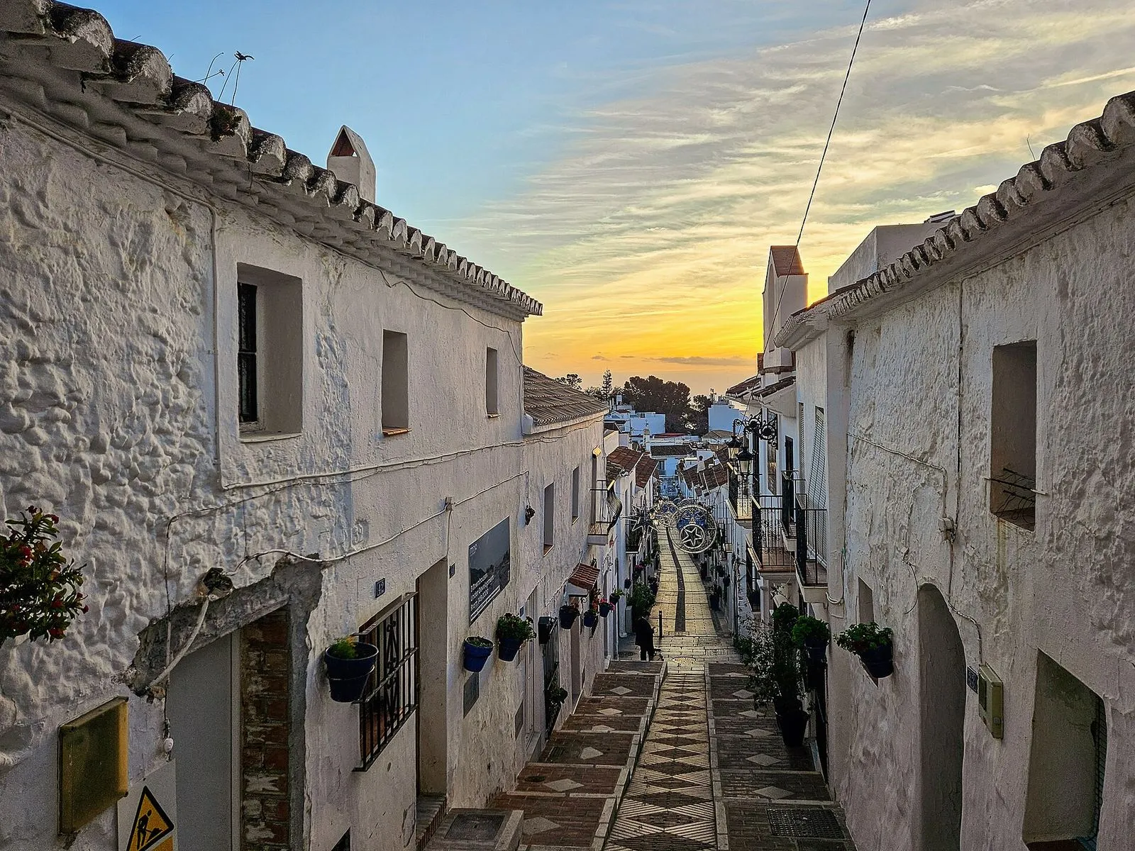 Die Calle San Sebastián in Mijas Pueblo bei Sonnenaufgang, eine steile Gasse mit weißen Häusern und blauen Blumentöpfen
