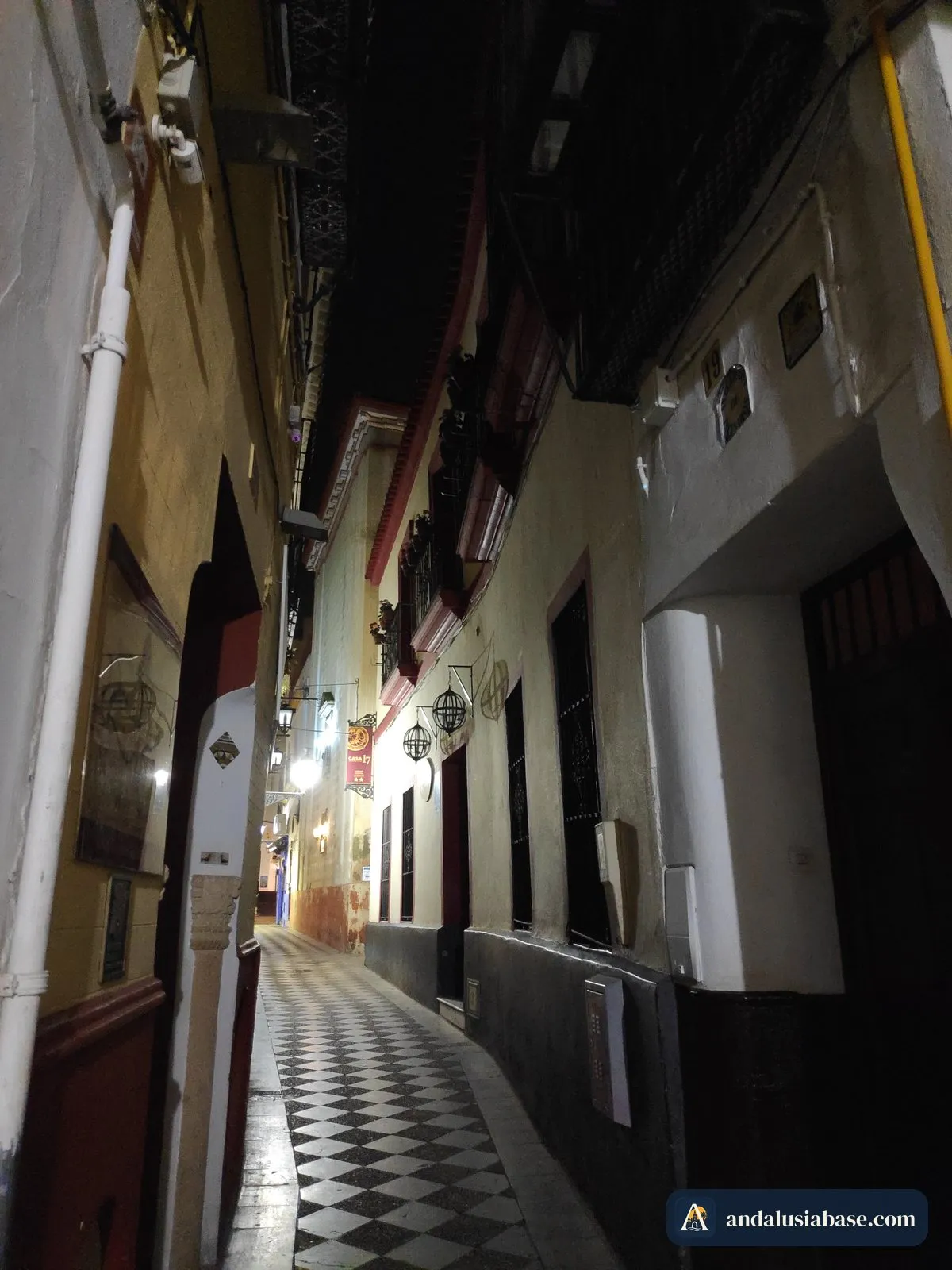 Uma ruela estreita de Santa Cruz à noite, iluminada por lanternas sobre um pavimento axadrezado