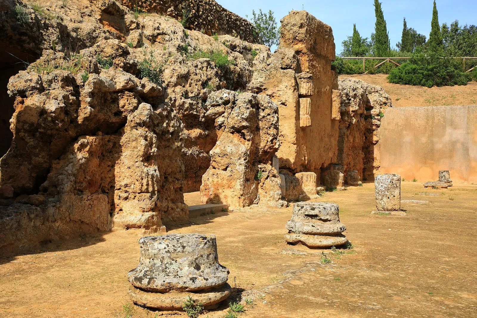 Stone tomb structures and column bases in the Roman Necropolis of Carmona, with cypress trees behind