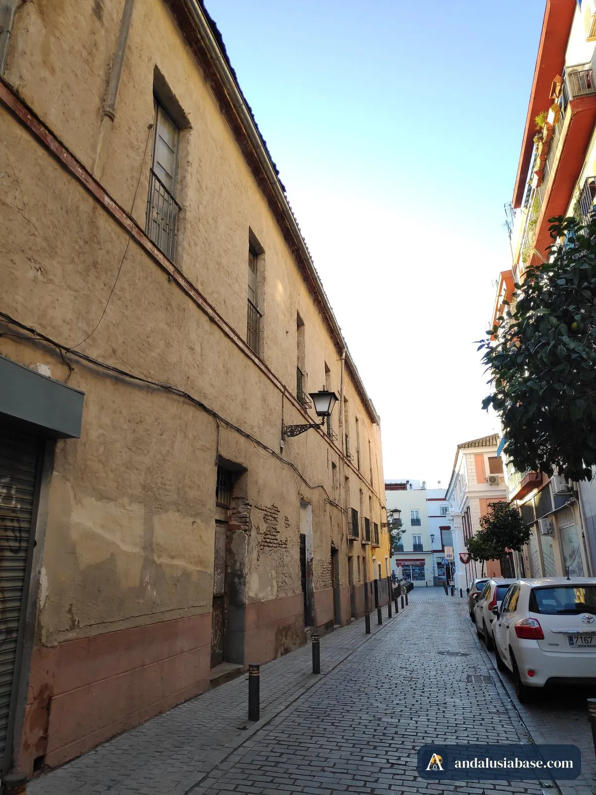 A quiet residential street of old houses and parked cars in Seville’s Macarena district