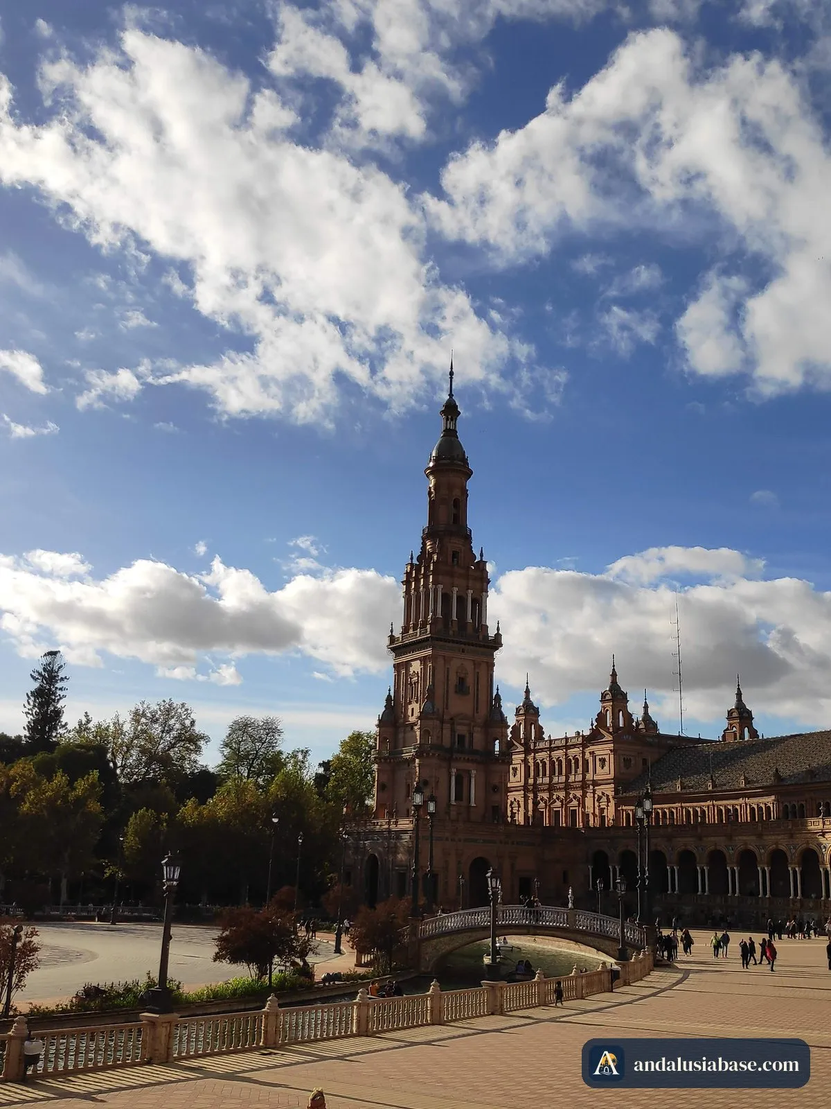 A torre e o palácio de tijolo da Plaza de España sob grandes nuvens brancas