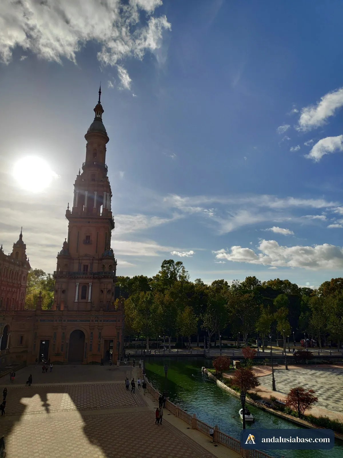 Uma torre da Plaza de España contra um céu azul intenso, com o sol a brilhar ao lado