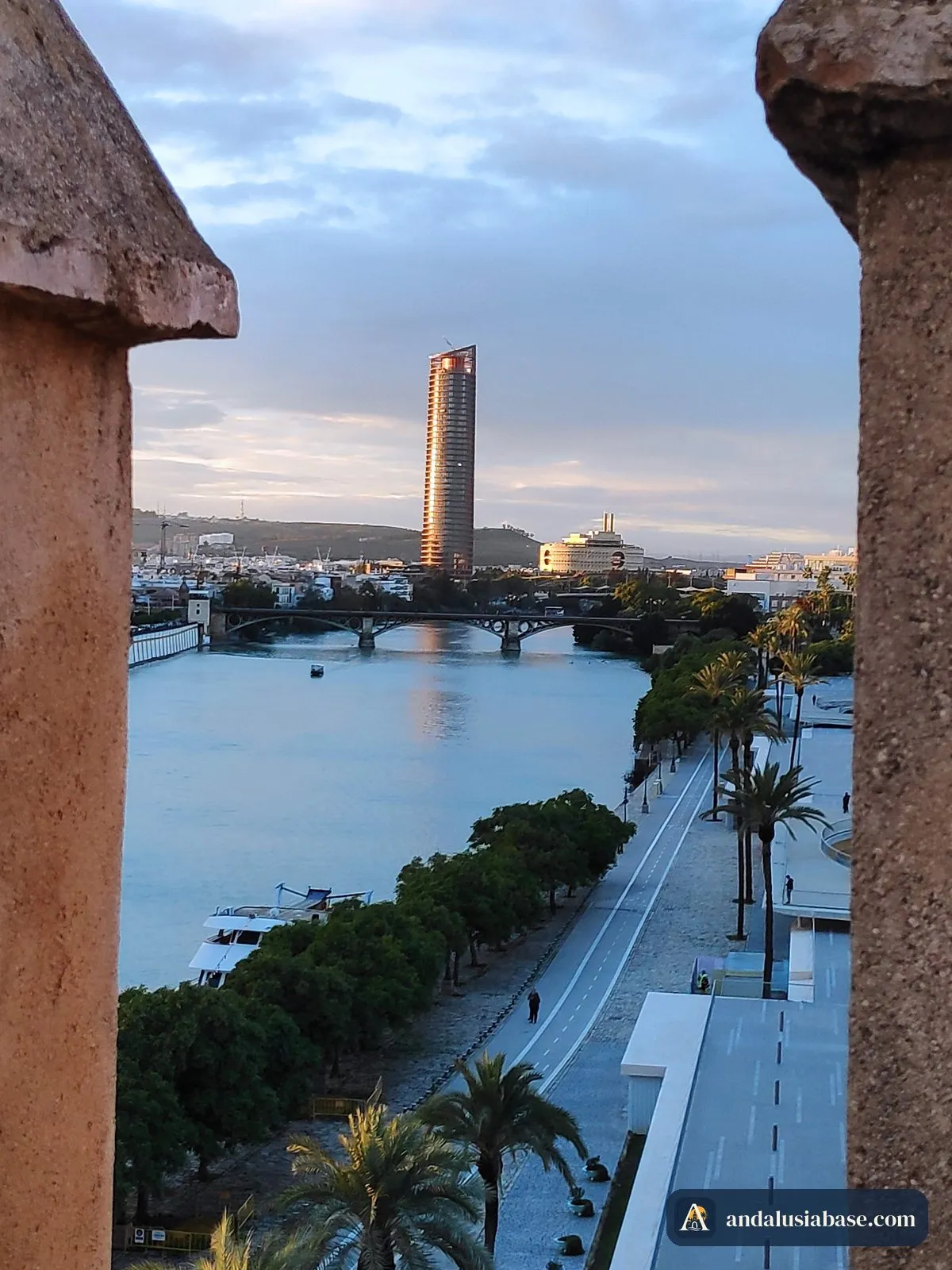 O Guadalquivir e o passeio ribeirinho para norte, vistos do alto da Torre del Oro entre duas ameias