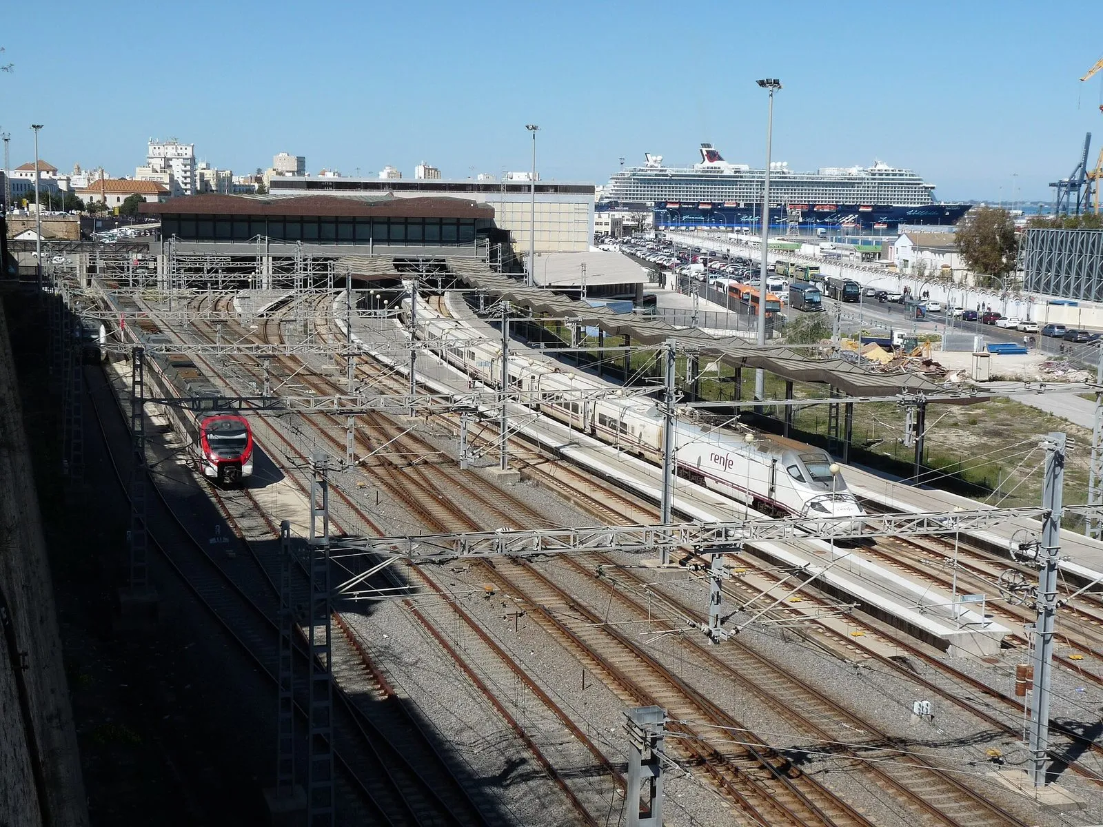 Railway lines at Cádiz station with a high-speed train and a cruise ship in the port behind