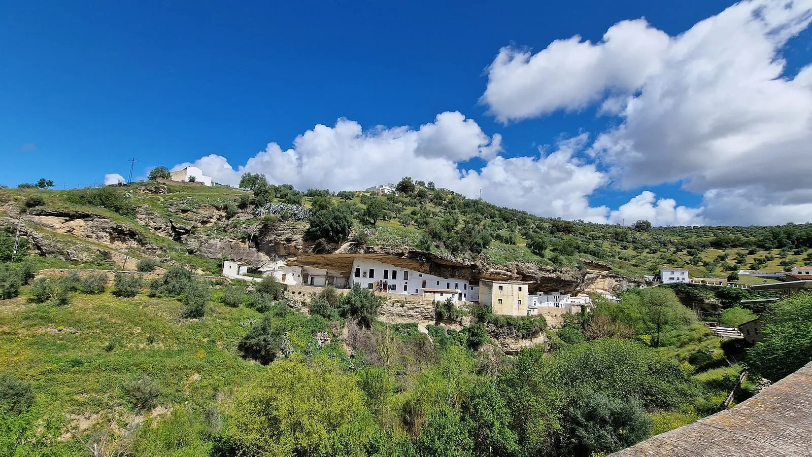 Setenil de las Bodegas mit weißen Häusern unter Felsüberhängen inmitten grüner Hügel