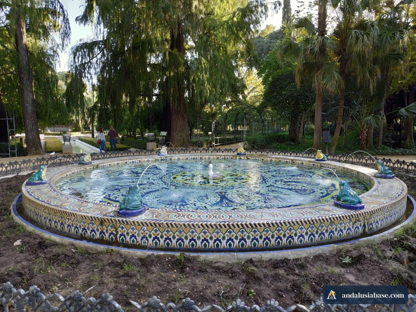 Fonte redonda decorada com azulejos azuis e amarelos entre palmeiras no Parque de María Luisa