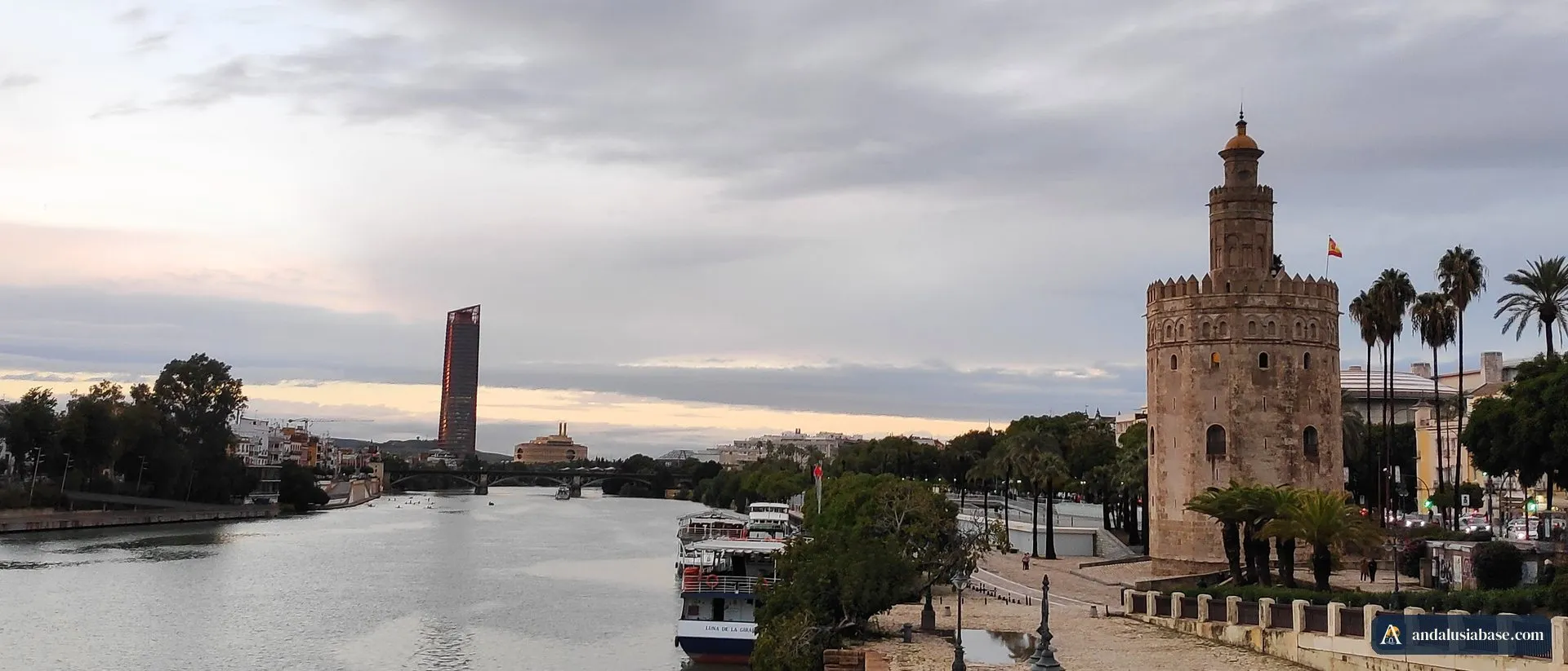 A Torre del Oro junto ao Guadalquivir numa tarde nublada, com os barcos turísticos atracados no cais