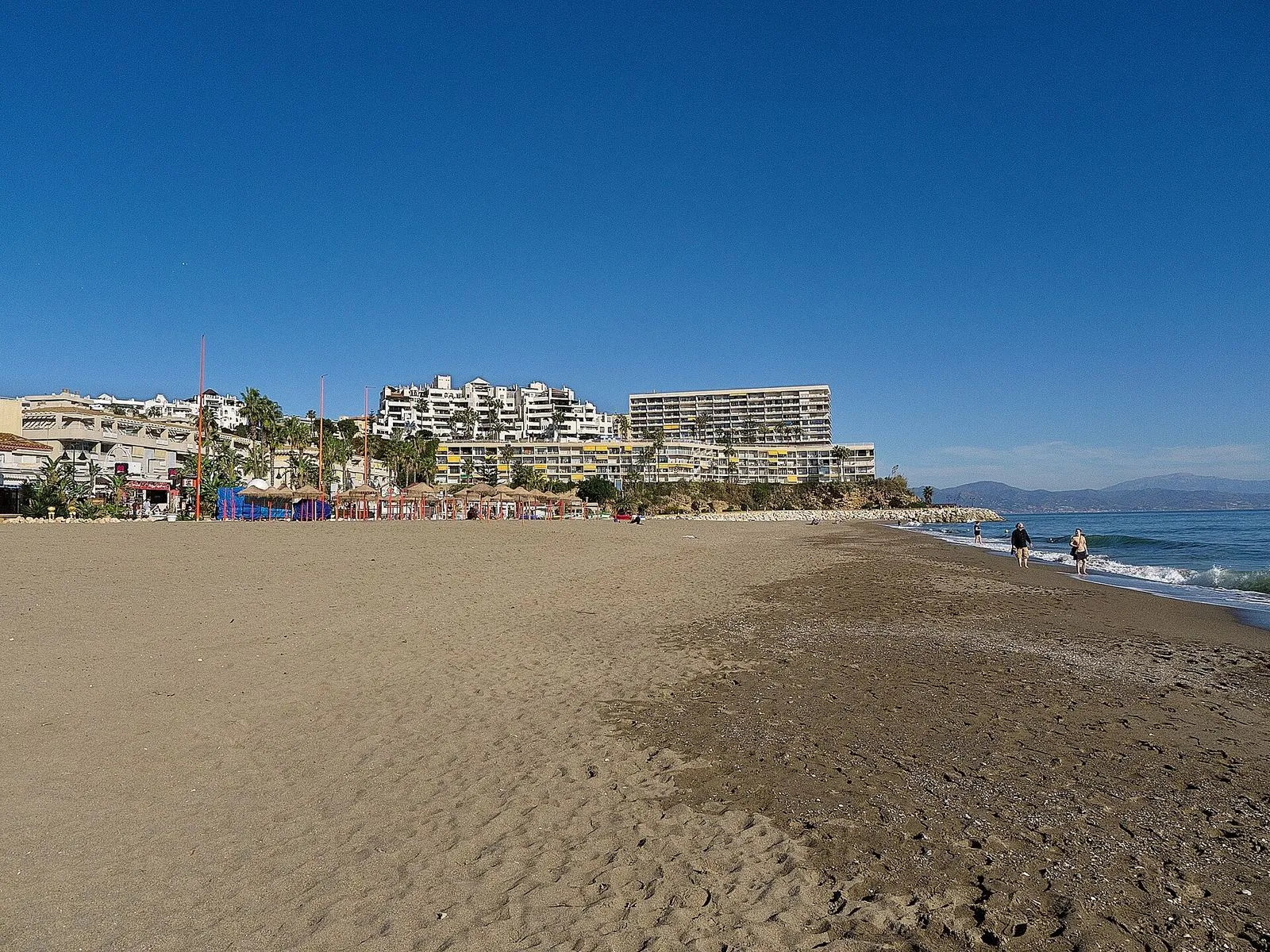 Der breite Sandstrand La Carihuela in Torremolinos unter klarem blauem Himmel