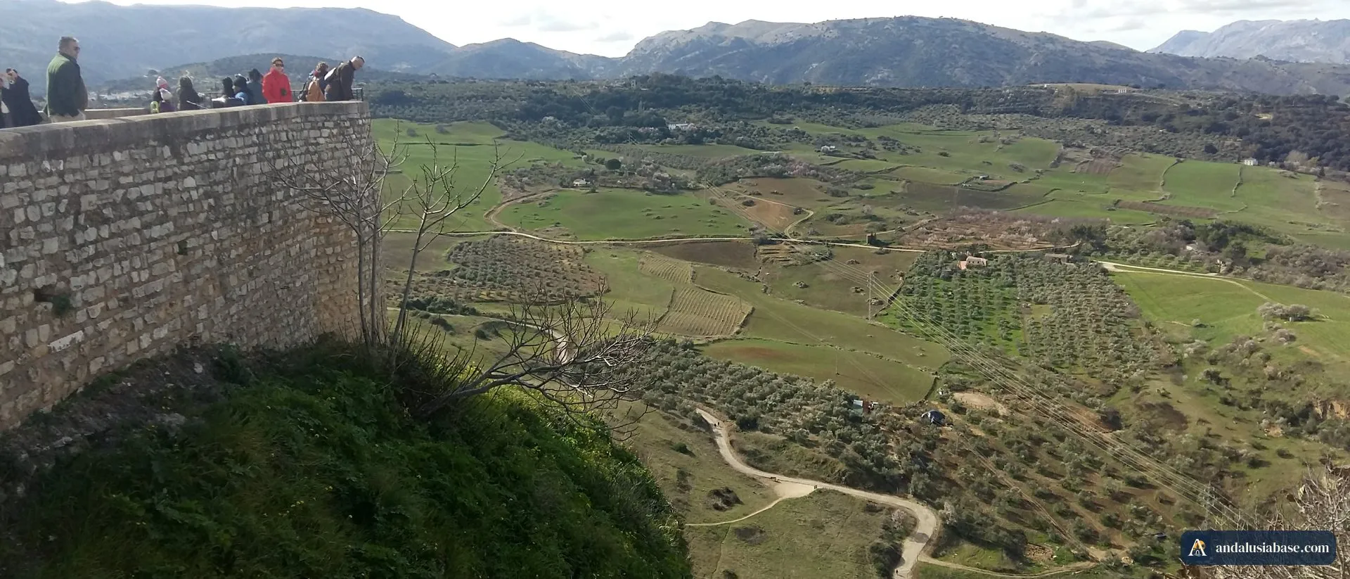Visitors at a cliff-top viewpoint in Ronda above green farmland and mountains