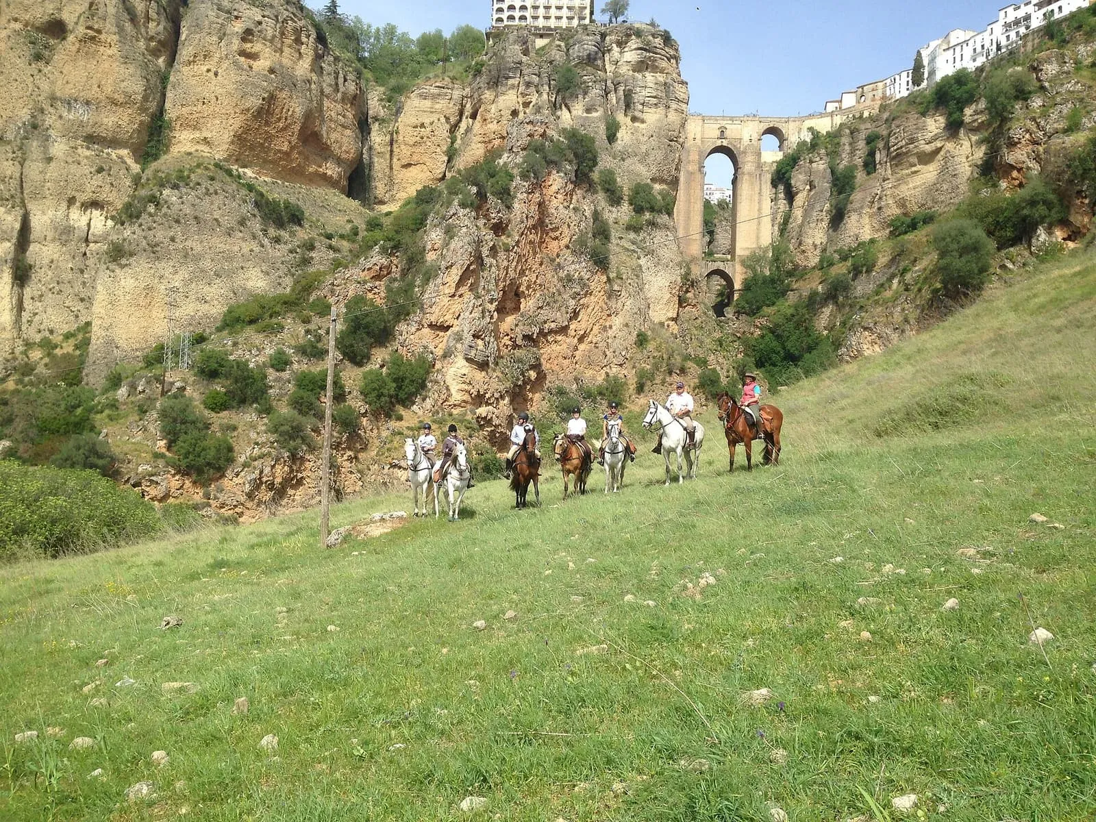 Jinetes cruzando un prado bajo el Tajo y el Puente Nuevo de Ronda