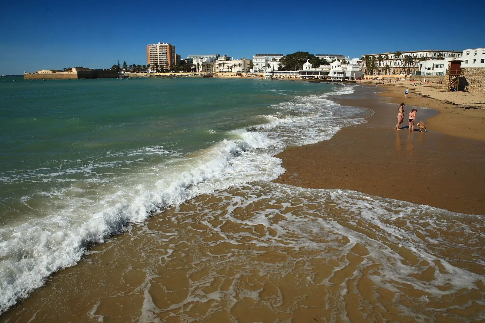 Waves on the sand of La Caleta beach in Cádiz under a clear blue sky