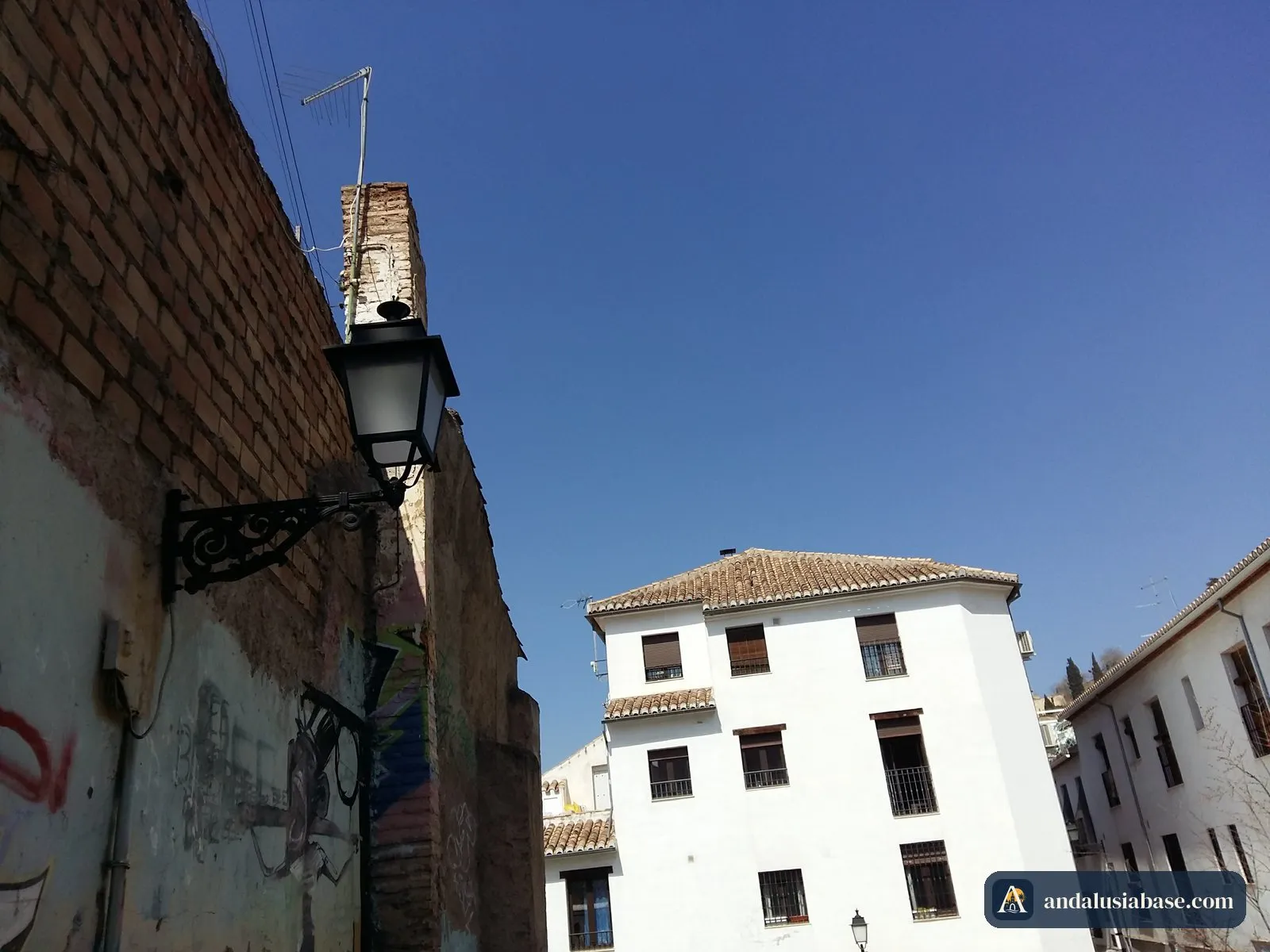 Um candeeiro de ferro num muro de tijolo diante de uma casa branca do Albaicín